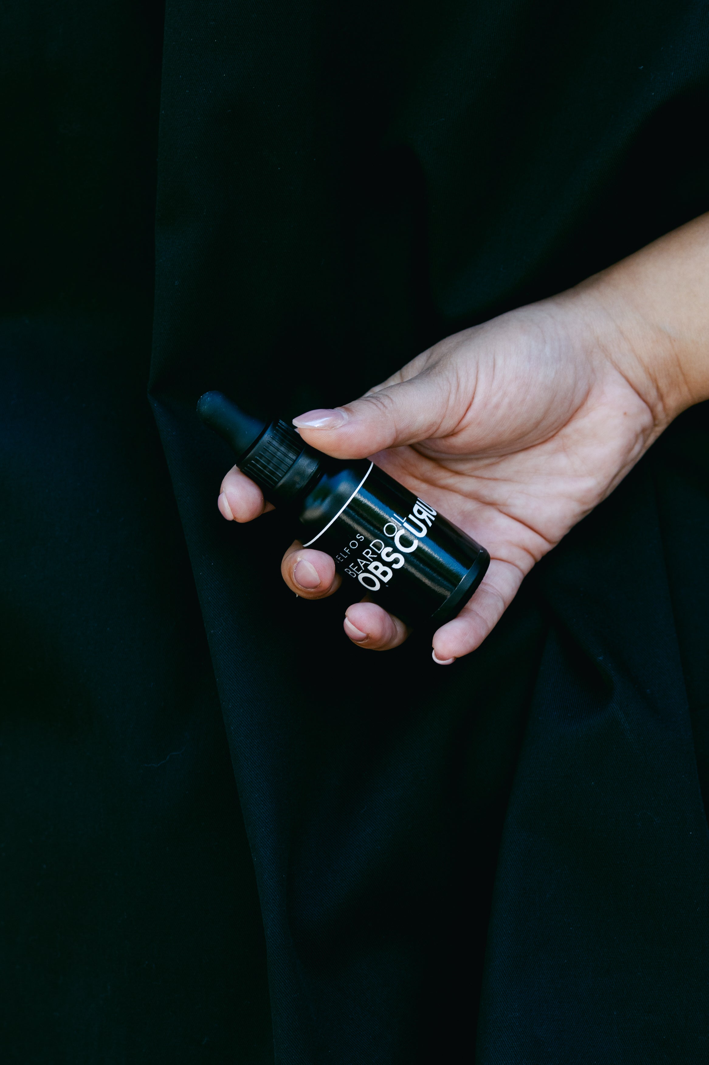Hand holding a black bottle with visible branding against a dark background