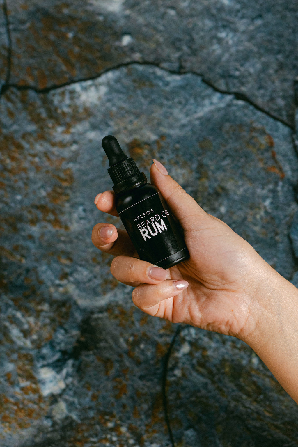 Hand holding a black bottle labeled 'Rum' against a textured stone background